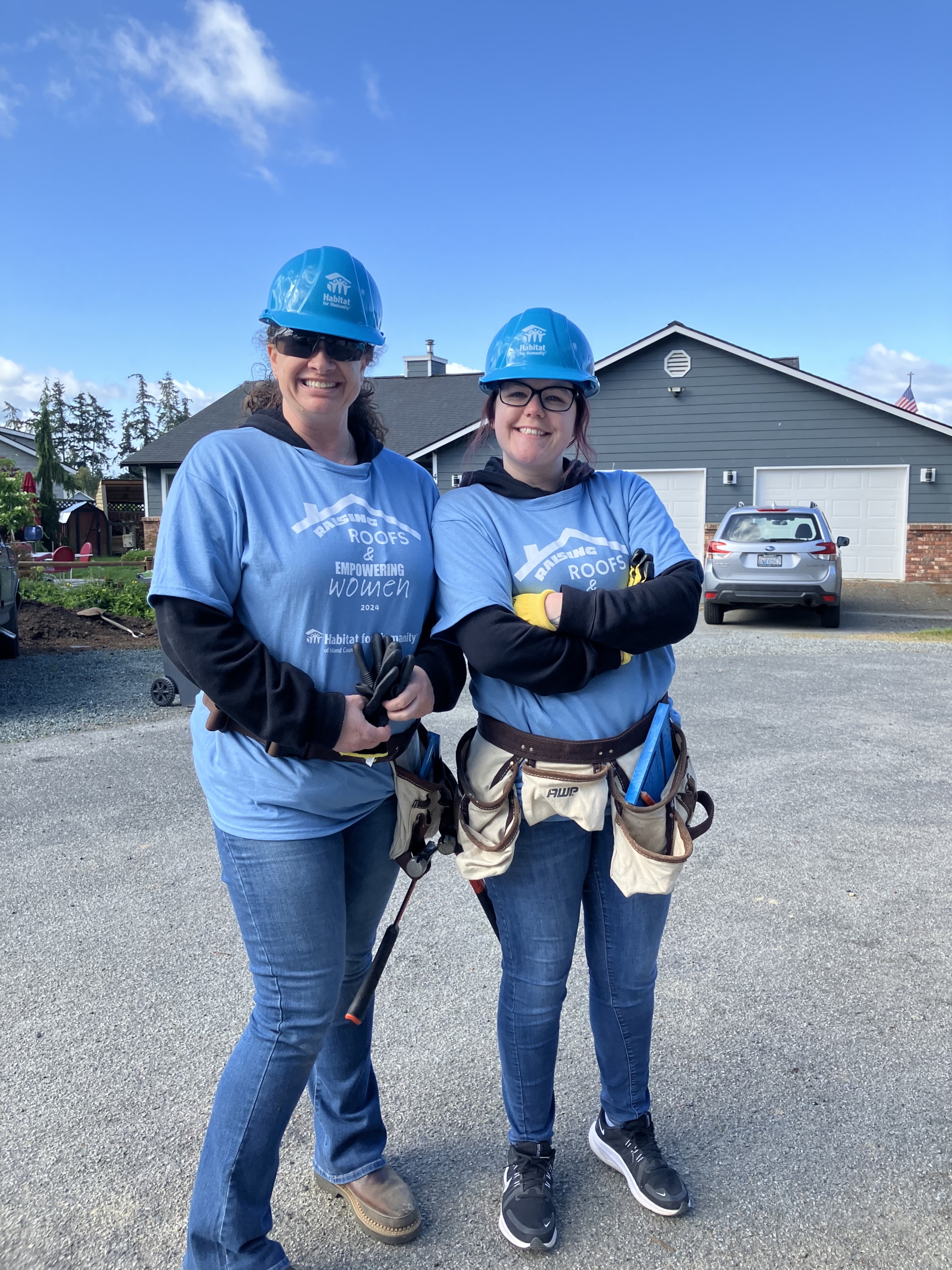 Two Skagit Habitat for Humanity Staff members standing side by side in blue hard hats and shirts at Island County Habitat for Humanity women build event.