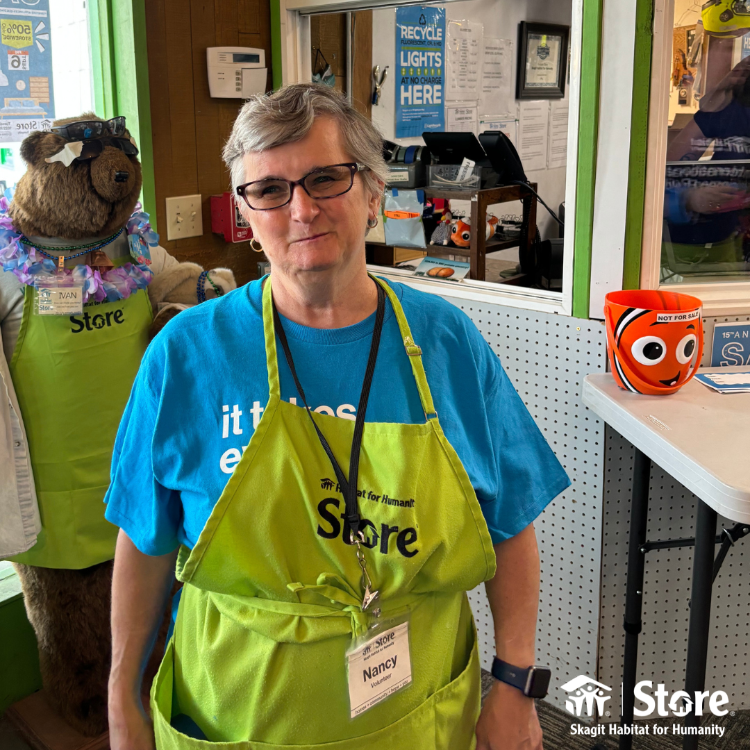 Nancy, a longtime volunteer at the Skagit Habitat for Humanity Store wearing a green Store Apron and Blue shirt.